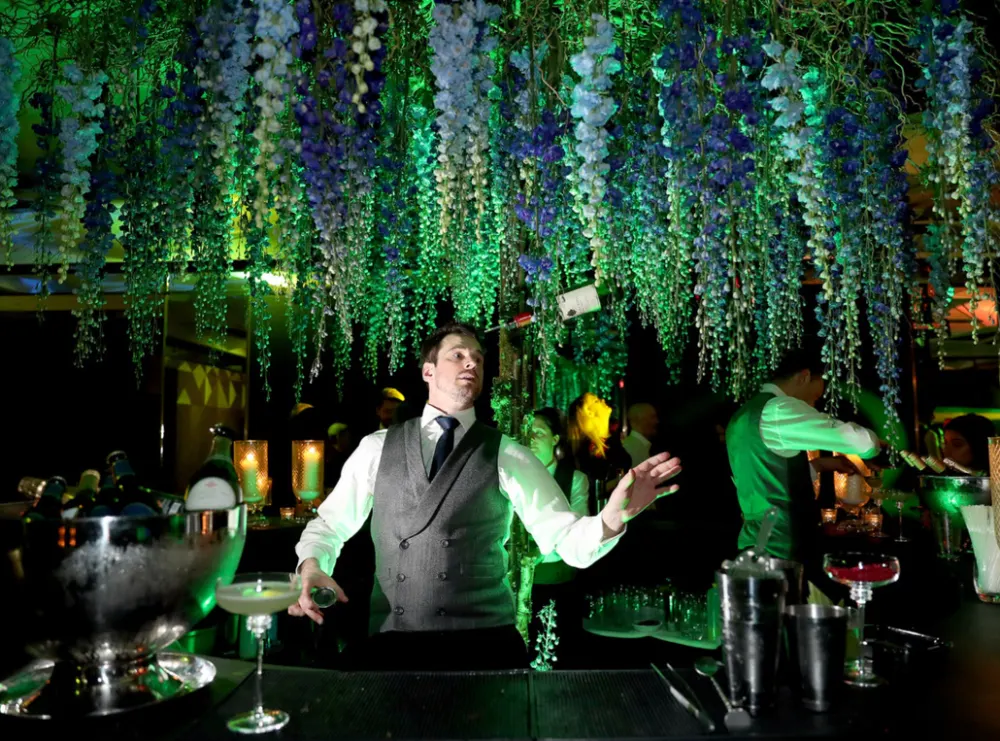 Cocktail maker serving guests beneath floral installations in a live event room
